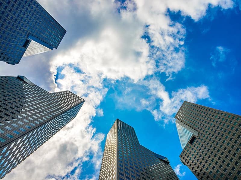 Três prédios altos espelhados com um céu bem azul e ensolarado, trazendo o contexto de empresas de fachada.